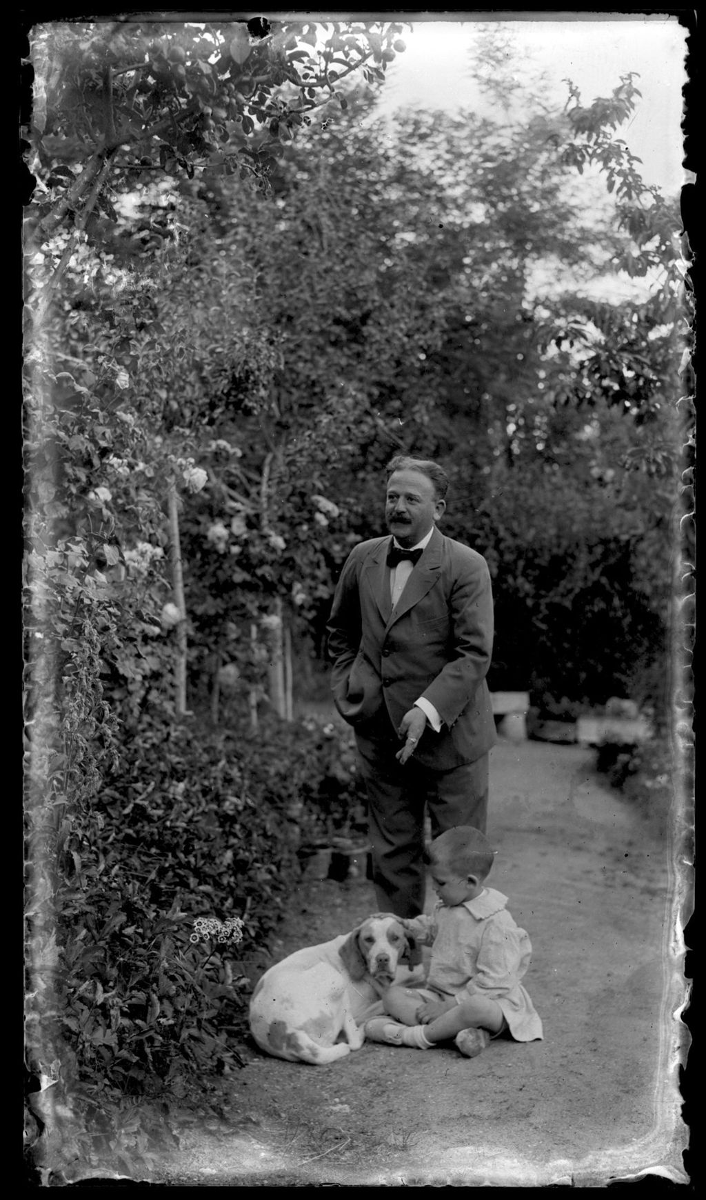 HOMBRE CON NIÑO Y PERRO EN EL JARDIN.