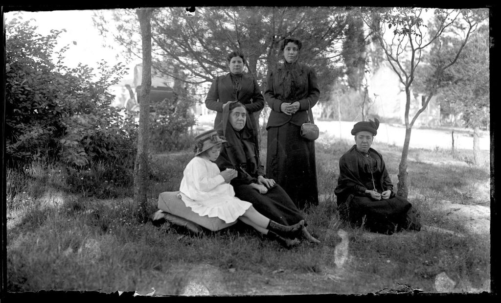 MUJERES DE NEGRO CON NIÑA Y CARRUAJE DETRÁS.